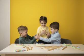 Three children engage in a playful educational lesson in a vibrant yellow classroom. Smiling faces