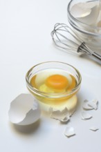 Egg whites and egg yolks in glass bowl and egg shells, whisk