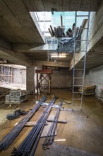 A construction site with steel beams, wooden planks, and a blue ladder. The area is lit naturally,