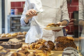 Chef wearing a white uniform carefully serving a fresh cinnamon roll onto a plate with tongs.