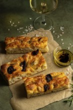 Freshly baked homemade focaccia topped with garlic and olives served on parchment paper.