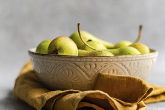 A rustic ceramic bowl filled with wild pears rests on a soft, golden cloth. The natural tones and