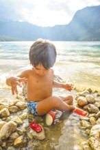 Young child enjoying summer vacation, playing with a toy car by the water's edge of lake bohinj in