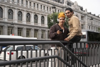 A gay couple in casual attire shares a tender moment on a Madrid street, leaning on a railing and
