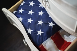 A folded American flag rests neatly inside a white wooden drawer, symbolizing national pride and