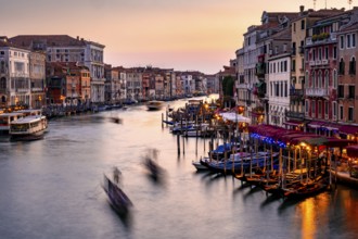 View of the Grand Canal with gondoliers at sunset, picturesque evening mood with illuminated