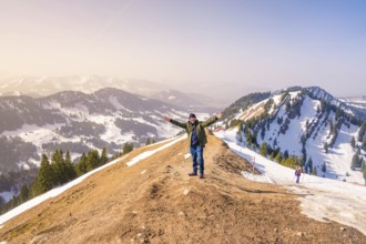 A hiker with outstretched arms enjoys the view from the mountain summit with deep snow and clear