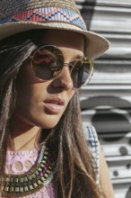 A fashionable woman wearing a straw hat and chic sunglasses. Her long hair and decorative necklace