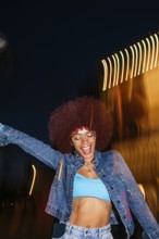 African descendant woman with vibrant afro hair joyfully dancing under night lights. Wearing