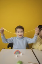 A child joyfully stretches colorful modeling clay during a creative lesson. The bright yellow