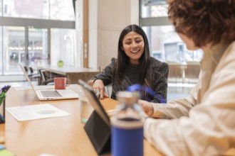 Colleagues discussing a project in a bright office space Laptops, documents, and a coffee mug are