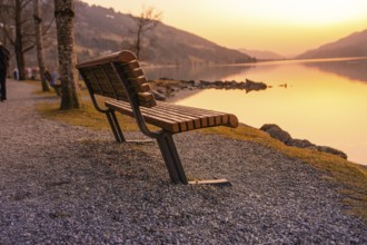 An empty wooden bench on the lakeside at sunset on a gravel path, Großer Alpsee, Immenstadt im