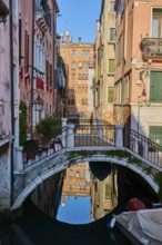 View from a gondola on a waterway in Venice going through the houses on a quiet and sunny morning