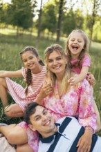 A joyful family shares a happy moment together in a lush green park, laughing and embracing. The