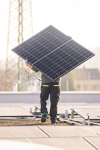 Person carrying solar module on a sunny roof next to a power pole, ready for installation, PV