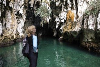 A woman stands at the edge of a cave, admiring the striking rock formations and vibrant turquoise