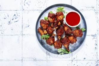 Crispy pieces of fried chicken, on a plate with sauce and herbs, in a modern kitchen environment,