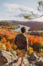 A person stands on a rocky overlook, admiring the vibrant autumn foliage in Quebec, Canada. The
