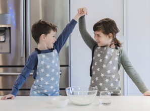 Two young siblings in star patterned aprons enthusiastically raise their hands in celebration while