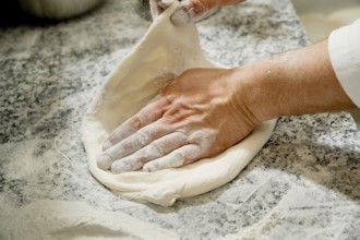 Cropped unrecognizable person kneading fresh pizza dough on a flour-dusted marble countertop,