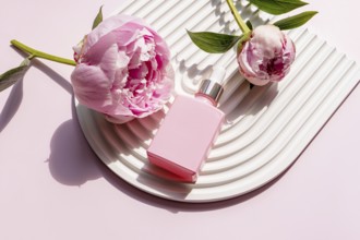 Pink cosmetic bottle alongside beautiful peonies on a stylish white corrugated plate. The floral