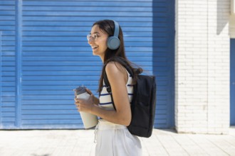 A woman enjoys city life outdoors, wearing headphones and carrying a water bottle, embodying an