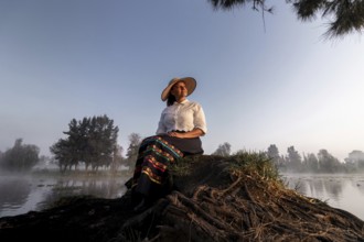 A woman in traditional attire enjoys a peaceful moment by the water in Xochimilco, Mexico.