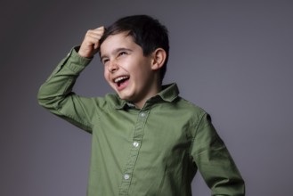 A young boy in a green shirt is laughing joyfully against a gray background. His expressive eyes