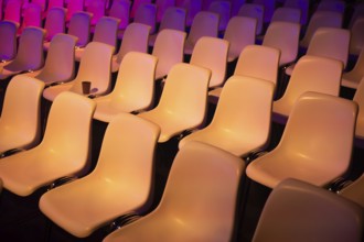 Rows of empty seats at a conference of AI in Amsterdam by vibrant purple and orange lights. The
