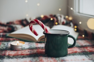 Cozy Christmas setting featuring a green mug, a festive candy cane, and a flickering candle next to