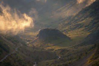 A stunning valley landscape at sunrise, with golden light illuminating mist and rugged hills in the