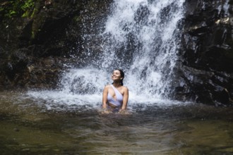 Young Ecuadorian woman enjoys blissfully in a natural pool under a waterfall in the Choco Andino