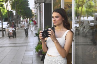 A young woman stands on a bustling city street, holding a camera She gazes ahead, ready to capture