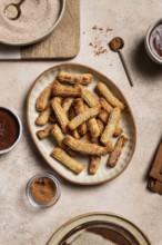 Top view of a ceramic plate filled with sugary churros next to bowls of chocolate sauce and