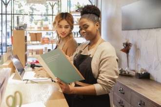 Two workers in a cosmetics store engage in tasks at the counter. One reads a catalog while the