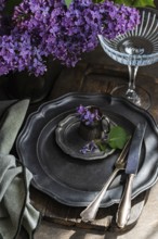 A rustic table setting features antique pewter plates and cutlery, adorned with vibrant lilac