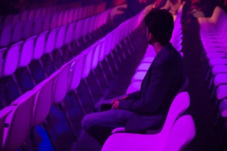 A indian man on a white chair in a spacious, purple lit auditorium at a conference of AI in