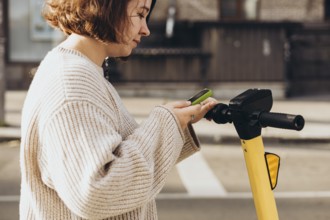 A woman is engaged in scanning a QR code with her smartphone to rent an electric scooter, standing