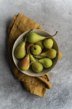 A top view of a ceramic bowl filled with fresh wild pears, set on a rustic surface with a brown
