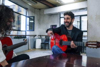 Male friends playing guitars at table in music studio