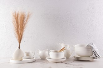 A minimalist interior design featuring elegant white tableware and a decorative vase with dried