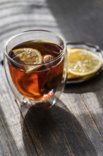 A warm glass of English tea, infused with a slice of lemon, presented on a rustic wooden table,