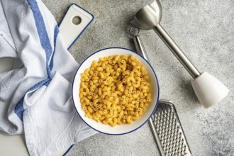 A bowl of chifferi rigati pasta sits on a counter top, accompanied by a grater, a mixer, and a dish