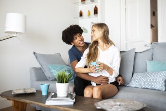 A couple sits together on a comfortable couch, sharing a warm moment with coffee. The bright and