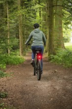 Person riding a bicycle in the forest. The surroundings are green and quiet, with a natural path,