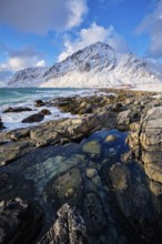 Beach of Norwegian sea on rocky coast in fjord on sunset in winter. Vareid beach, Lofoten islands,