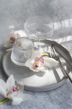 A refined dining setup featuring ribbed glassware, delicate orchids, and sleek cutlery on a
