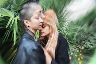 A lesbian couple shares a tender, intimate moment surrounded by vibrant greenery, symbolizing love