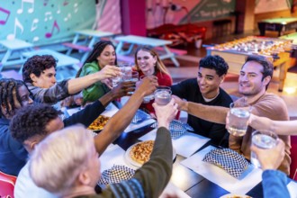 Group of cheerful multi ethnic friends toasting drinks while enjoying a meal together at a bowling