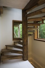 Brown stained cherry wood spiraling staircase with thin flat wooden steps attached to pine wood